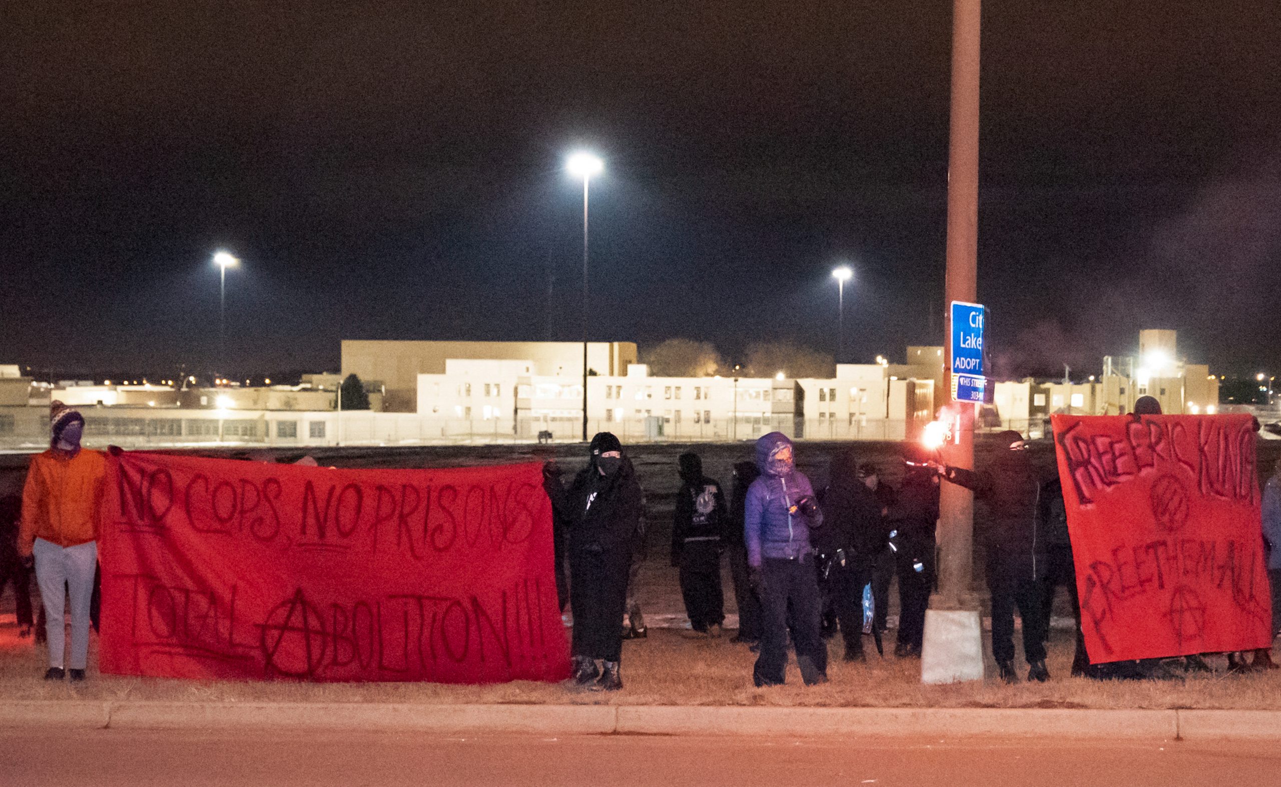 Protesters stand on the side of the road with banners and road flares